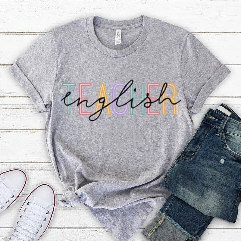 Front view of a stylish 'English Teacher' t-shirt in grey, featuring bold black lettering overlaying colorful 'Teacher' text. Perfect for showcasing your passion as a cute teacher t-shirt. Shop today at TeachingTeez.com!