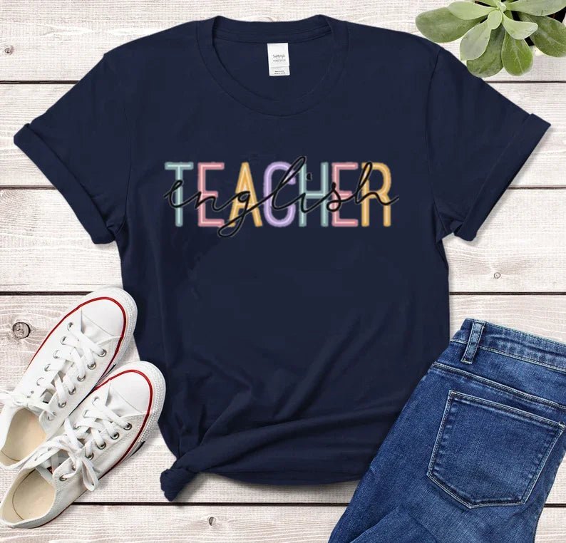 Front view of a stylish 'English Teacher' t-shirt in navy, featuring bold black lettering overlaying colorful 'Teacher' text. Perfect for showcasing your passion as a cute teacher t-shirt. Shop today at TeachingTeez.com!