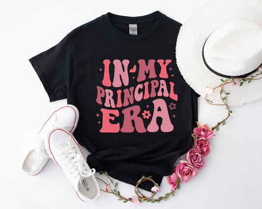 Flat lay of the "In My Principal Era" t-shirt featuring retro pink groovy text on a soft, high-quality black fabric – perfect for school principals stepping into their leadership role.