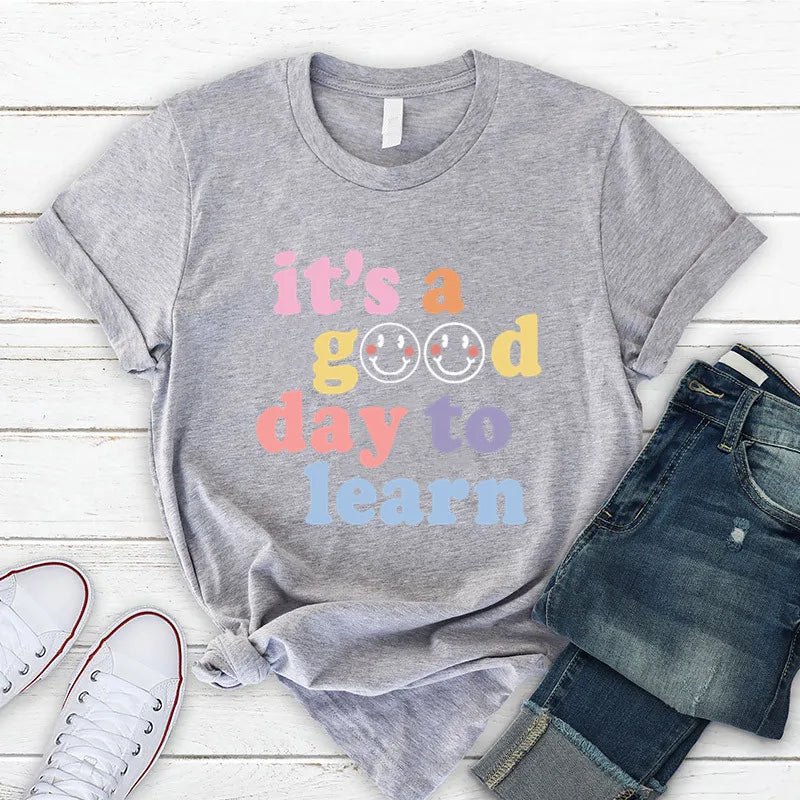 Gray shirt Flat lay of the "It's a Good Day to Learn" t-shirt featuring colorful, playful lettering with smiley faces in the "O"s of "Good," crafted from soft fabric for comfort—shop today and spread positivity!