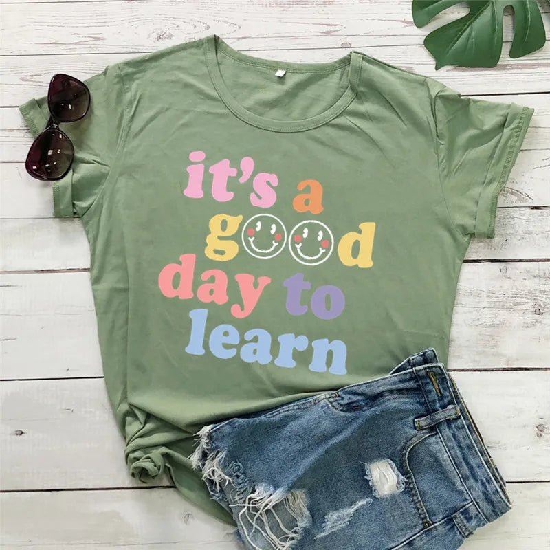 Army Green shirt Flat lay of the "It's a Good Day to Learn" t-shirt featuring colorful, playful lettering with smiley faces in the "O"s of "Good," crafted from soft fabric for comfort—shop today and spread positivity!