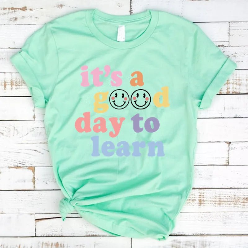 Turquoise shirt Flat lay of the "It's a Good Day to Learn" t-shirt featuring colorful, playful lettering with smiley faces in the "O"s of "Good," crafted from soft fabric for comfort—shop today and spread positivity!