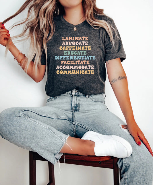 A woman wearing a dark gray "Laminate, Advocate, Caffeinate, Educate, Differentiate, Facilitate, Accommodate, Communicate" t-shirt from TeachingTeez.com. The colorful text highlights the key roles of inclusive educators. Perfect for teachers supporting diverse learners, order this shirt from TeachingTeez.com to show your dedication to inclusive education!